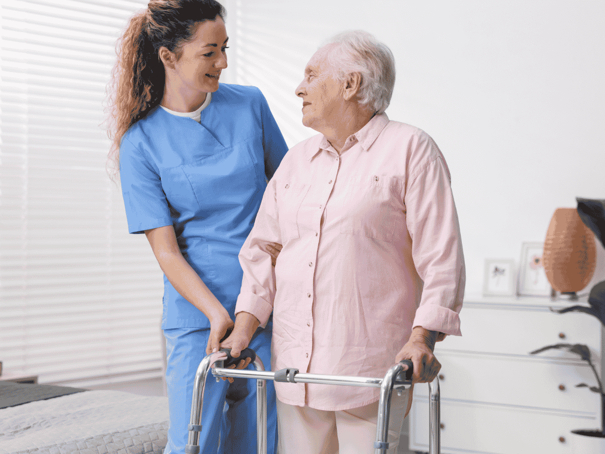 Caregiver helping a senior walk with a walker while recovering at home