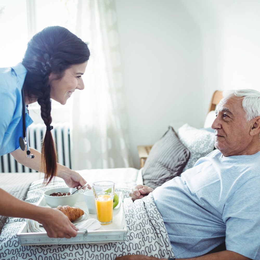 Caregiver serving breakfast to a senior man at home